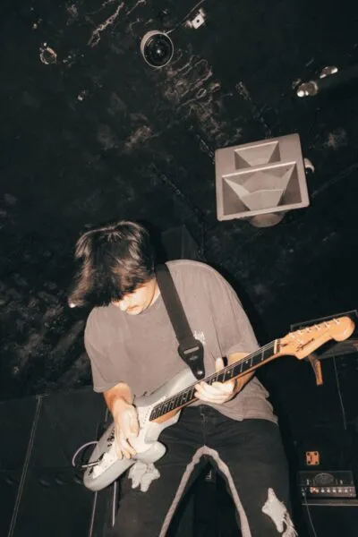 Guitarist playing intensely on stage — Focused guitarist performing dynamically at a small venue, spotlight highlighting movement and raw musical energy.