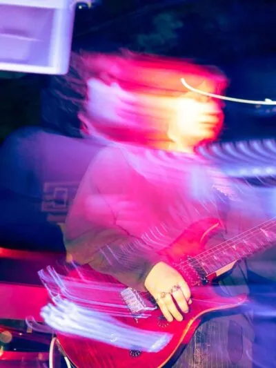 GRLBND Guitarist in motion under purple lighting, blurred dynamic effect highlighting energy and movement during live performance on stage.