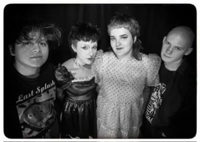 Black-and-white portrait of The Maisonettes posing closely, each with distinct expressions and alternative fashion styles against dark backdrop.