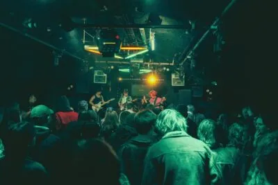 Live gig crowd from behind — Dark venue packed with an excited crowd watching a band perform on stage under vibrant neon lighting.