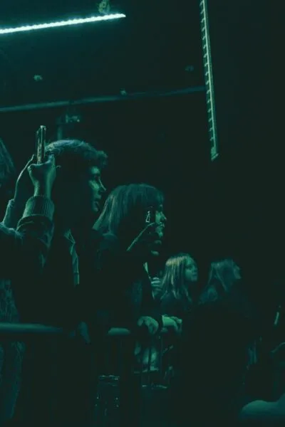Fans at gig front row — Audience members holding phones and watching a live show, capturing the energetic vibe of the intimate venue.