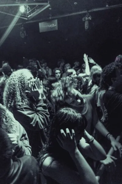 Live gig crowd from behind — Dark venue packed with an excited crowd watching a band perform on stage under vibrant neon lighting.