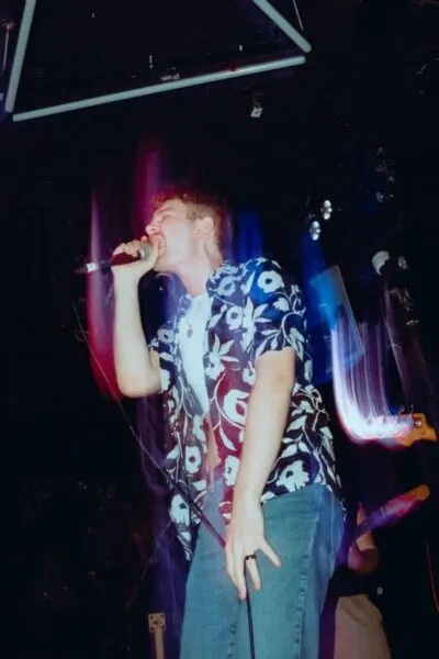 Singer with microphone, colourful stage lights — Frontman gripping microphone, singing passionately with vibrant lighting effects enhancing the immersive gig atmosphere.