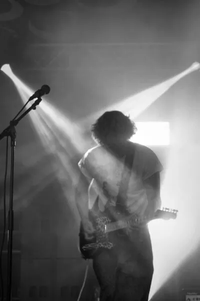 Elliott Plance - guitarist performing on stage in dramatic lighting with smoke and beams of light behind them.