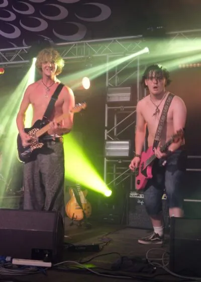 The Kabins' Elliott and Freddie perform energetically on stage under bright yellow lights.