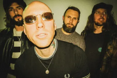 Four men posing together, Scott Anchors wearing sunglasses in the foreground, others behind with beards and hats.